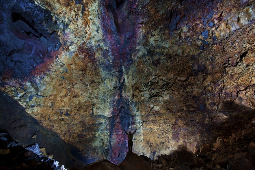 Person standing inside Thrihnukagigur volcano magma chamber in Iceland, showing colorful rock walls and vast underground space
