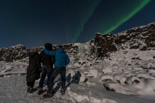 Grupa podróżników w Parku Narodowym Thingvellir zachwyca się pokazem zorzy polarnej.