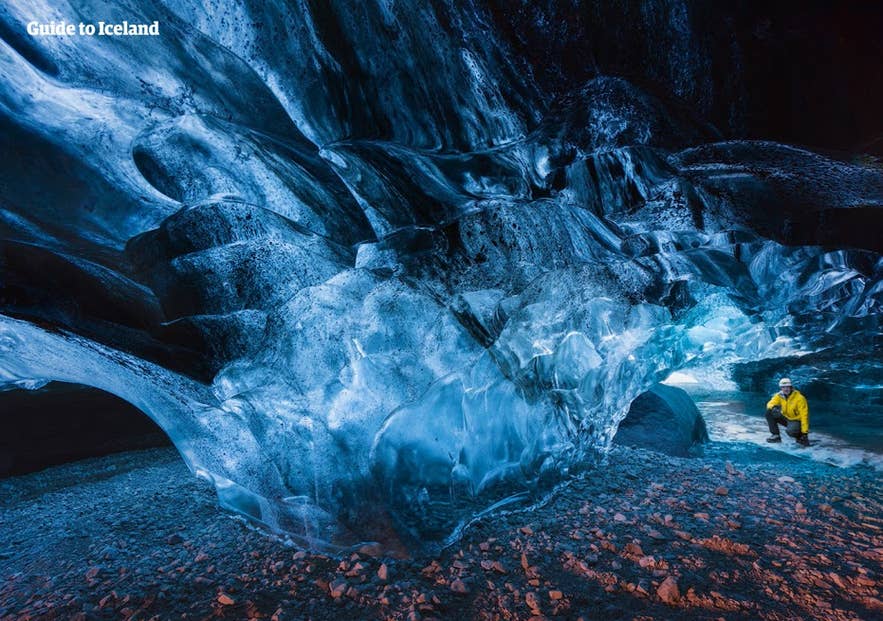 Visitor crouching at the back of a blue ice cave over reddish gravel, the ice the study's freeze-thaw terms describe.