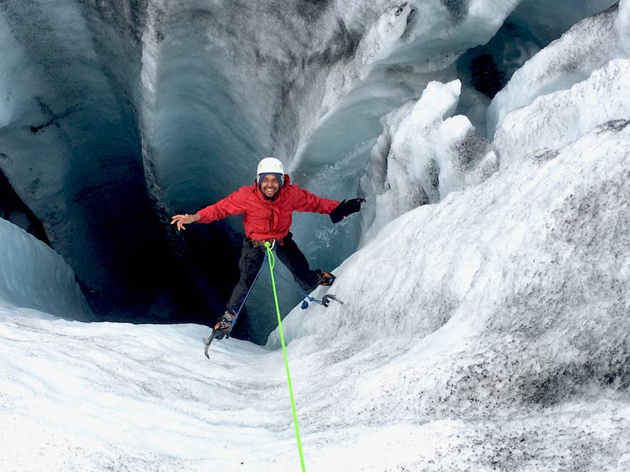 Montañista sonriente desciende a una cueva de hielo con cuerda y crampones durante una excursión por un glaciar en Islandia en julio.