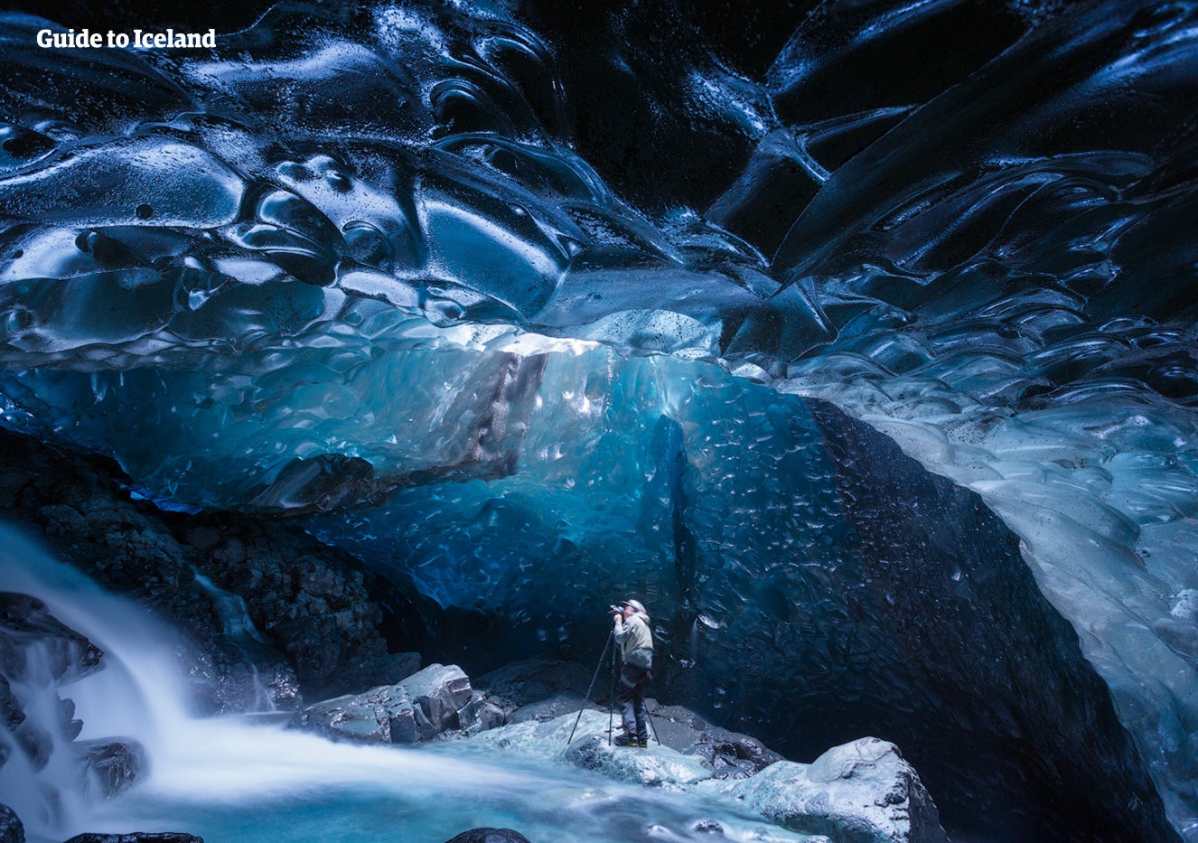 Persona all’interno di una grotta di ghiaccio blu in Islanda, sotto ghiaccio scolpito dal ghiacciaio con un fiume che scorre nella grotta.
