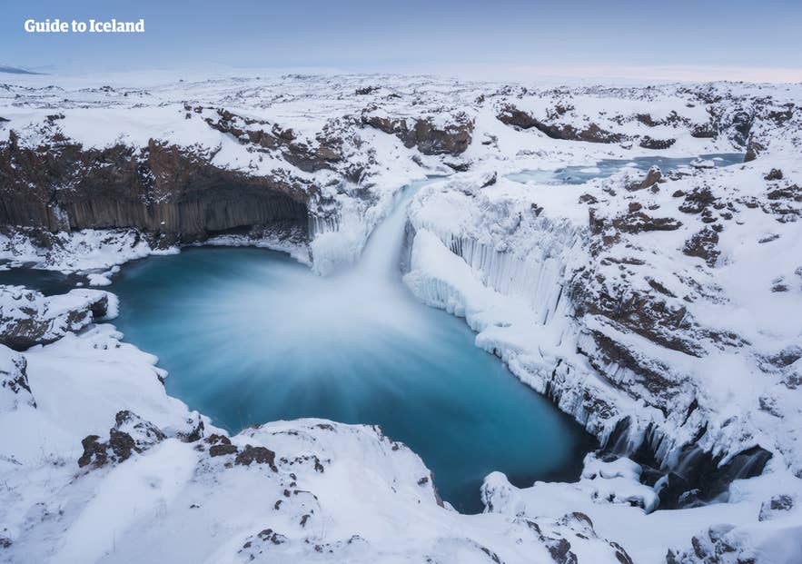 Aldeyjarfoss waterval gedeeltelijk bevroren tussen sneeuw en ijs in Noord-IJsland in november, toont typische winterse neerslag en weersomstandigheden.