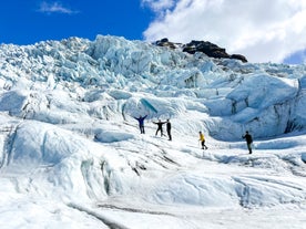 A group of people are standing on a glacier in Skaftafell, Iceland, wearing crampons and helmets for safety.