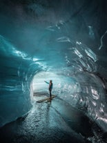 Eine Frau steht in der Katla-Eishöhle und trägt einen wasserdichten Mantel und Helm.