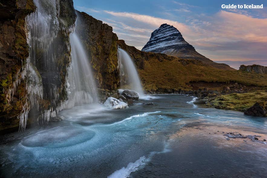 Frozen Kirkjufellsfoss waterfall with icy river in front of iconic Kirkjufell mountain at sunset in winter, a famous landmark on Iceland’s Snæfellsnes Peninsula.