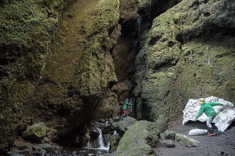 冰岛Raudfeldsgja峡谷内部的苔藓岩壁、溪流，以及探索狭窄峡谷的游客。