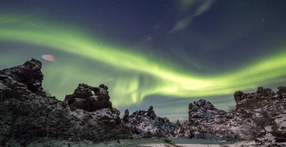 En strime av nordlys på himmelen over noen forrevne fjellformasjoner på Island.