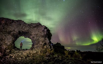 Nordlyset viser sig i grønt og lilla over en klippebue på Island.