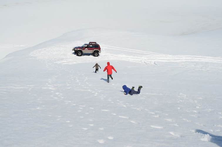 Three people running to a super jeep in the snow, one has fallen face down.