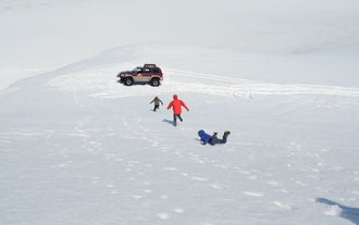 Three people running to a super jeep in the snow, one has fallen face down.