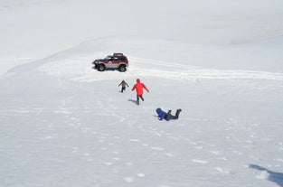 Tre personer rusar tillbaka till sin superjeep genom snön, en har ramlat med ansiktet före