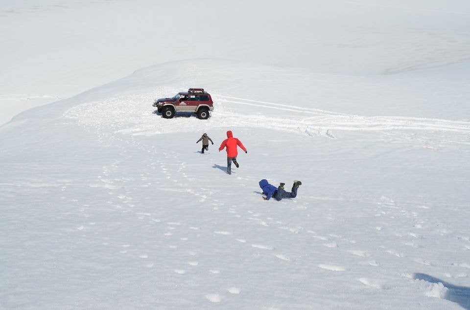 Trois personnes courant vers une Super Jeep dans la neige, l'une d'elles est tombée face contre terre.