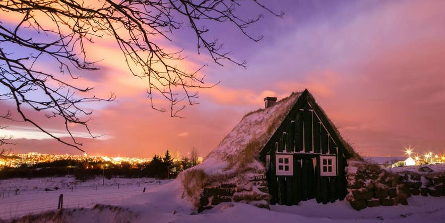 Snow-covered turf house at Arbaer Open Air Museum in Reykjavik at a pink winter sunset, in a coldest month above freezing.