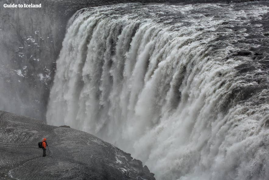 Persoon staat bij de Dettifoss-waterval in Noord-IJsland, een van Europa's krachtigste watervallen, omringd door mist en kliffen.