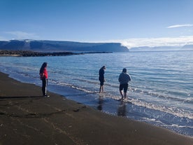 People paddle in the waters of a black sand beach with mountains in the distance at the Hornstrandir Nature Reserve in the Westfjords.