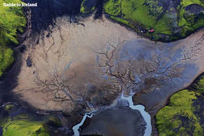 Green, mossy hills surround a black desert in the Icelandic Highlands.