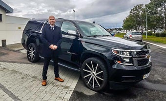 A professional chauffeur wearing a suit stands outside a luxury SUV.