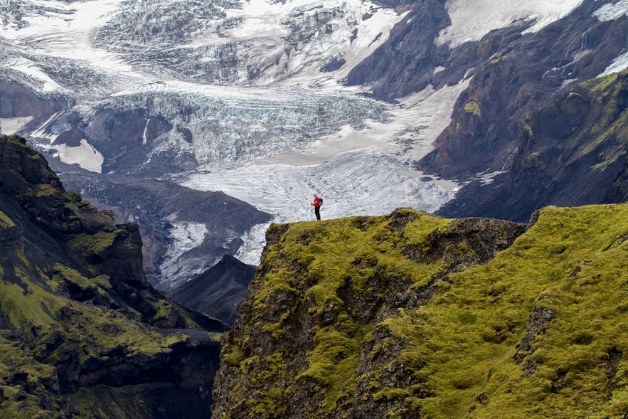 Hiker standing on a mossy cliff above a glacier tongue on the Laugavegur Trail