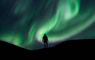 A person stands as the northern lights surround them in Iceland.