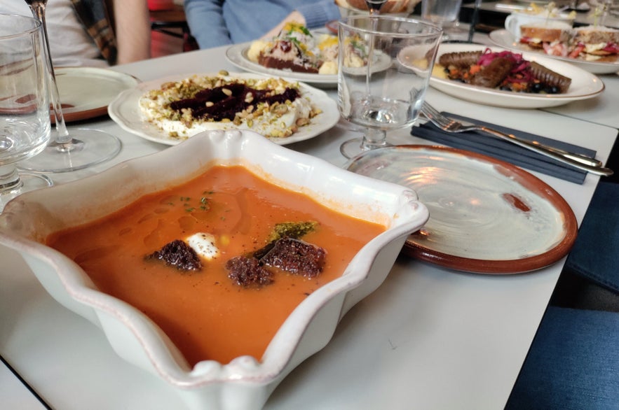 Rich tomato soup topped with cream and croutons, surrounded by shared plates at Litli Barinn. Rich tomato soup topped with cream and croutons, surrounded by shared plates at Litli Barinn.