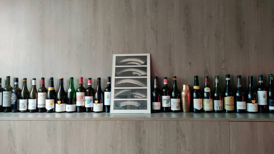 Wandpresentatie van wijnflessen en moderne kunst boven een houten kast bij restaurant Litli Barinn. Wandpresentatie van wijnflessen en moderne kunst boven een houten kast bij restaurant Litli Barinn.