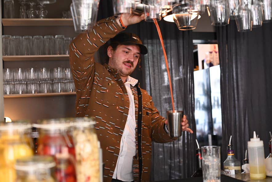 Barman bij Litli Barinn schenkt een cocktail in met flair aan de bar, omringd door potten met huisgemaakte infusies. Barman bij Litli Barinn schenkt een cocktail in met flair aan de bar, omringd door potten met huisgemaakte infusies.
