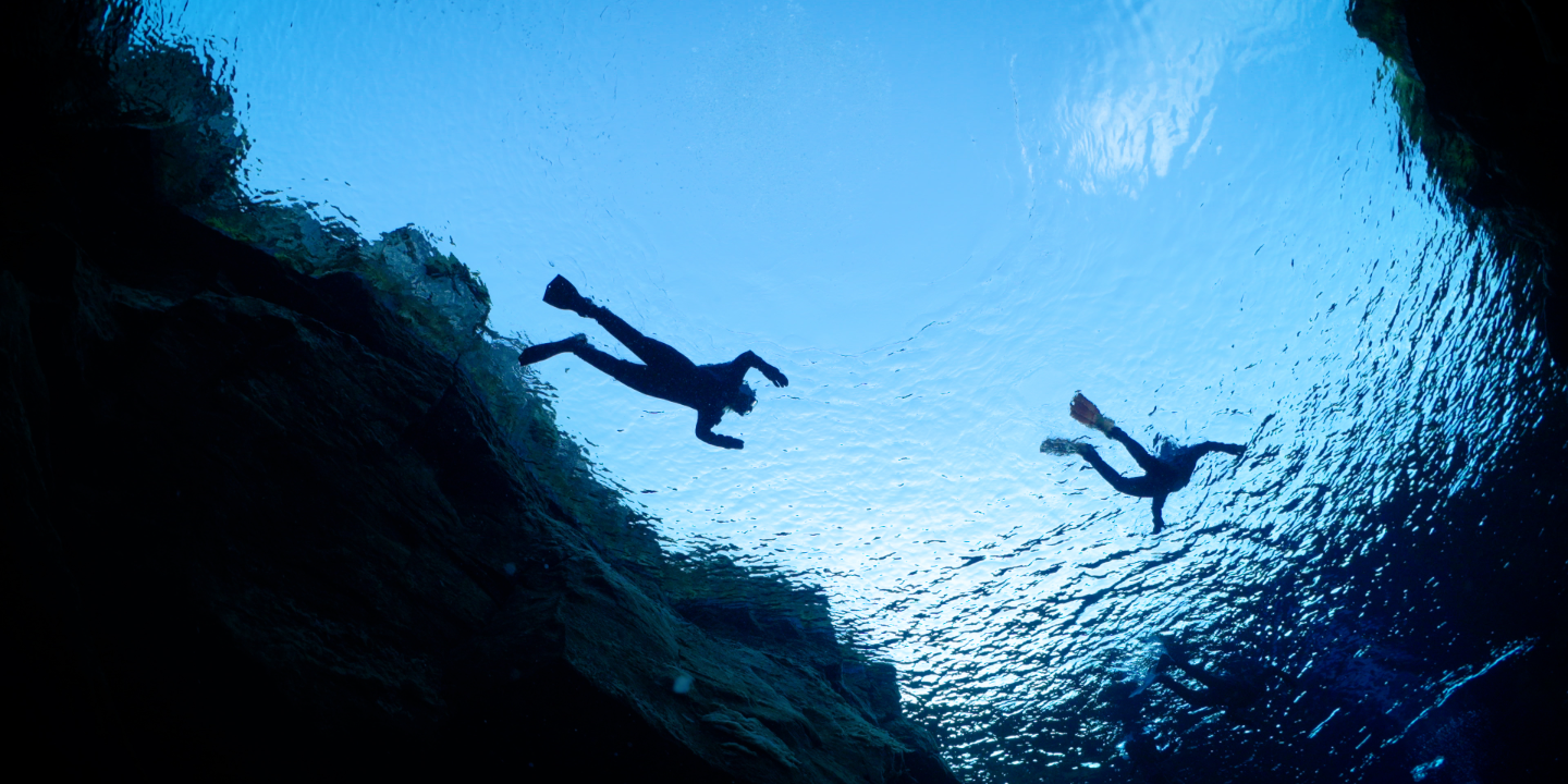 Vue sous-marine de la silhouette de plongeurs faisant du snorkeling et flottant près des falaises rocheuses de la faille de Silfra en Islande.