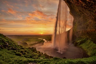 The midnight sun in Iceland casting its golden light upon the iconic South Coast waterfall Seljalandsfoss.