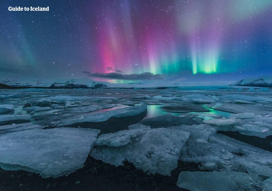 星空の下、ヨークルスアゥルロゥン氷河湖に浮かぶ氷とカラフルなオーロラ。