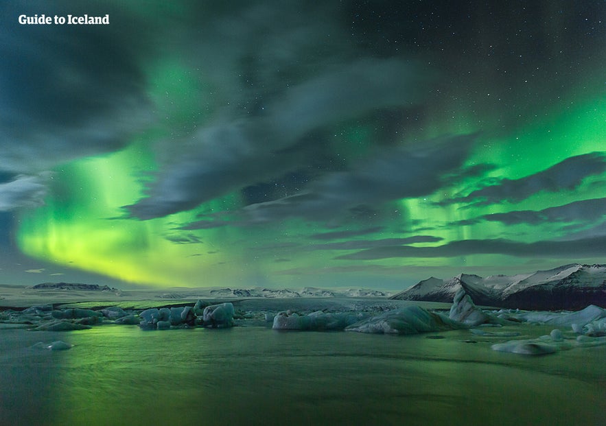 Northern lights over Jokulsarlon Glacier Lagoon in Iceland, with icebergs floating under a glowing green sky.