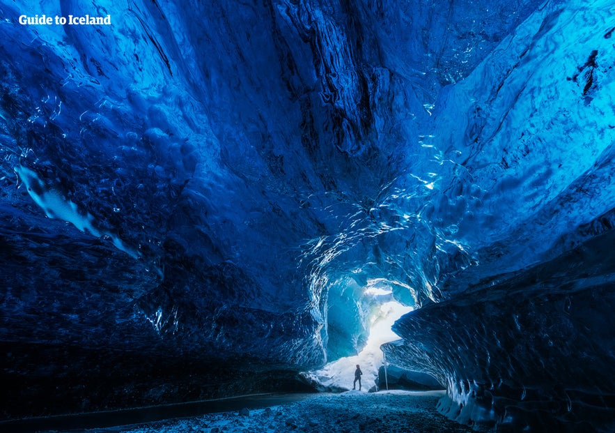 Person standing inside vivid blue ice cave in Iceland, showcasing crystal formations and shimmering glacial walls.