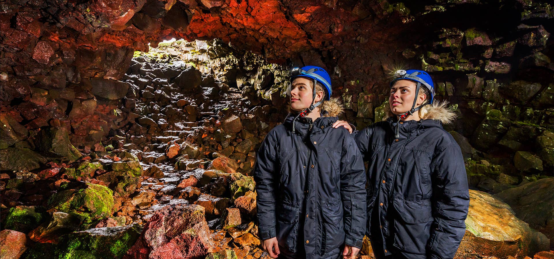 Two people wearing head torches look up on a lava tunnel tour.