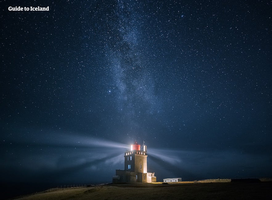 The lighthouse at Dyrhólaey shining under a starlit sky.