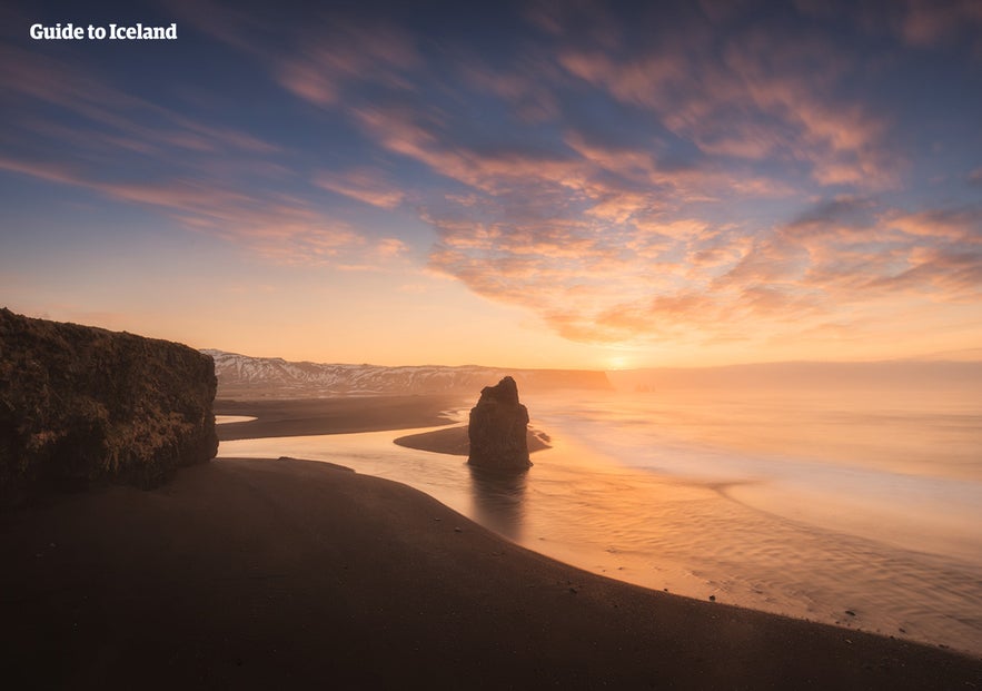 Den svarte sandstranden Reynisfjara. Du kan se steinsøylen Reynisdrangar midt på bildet.