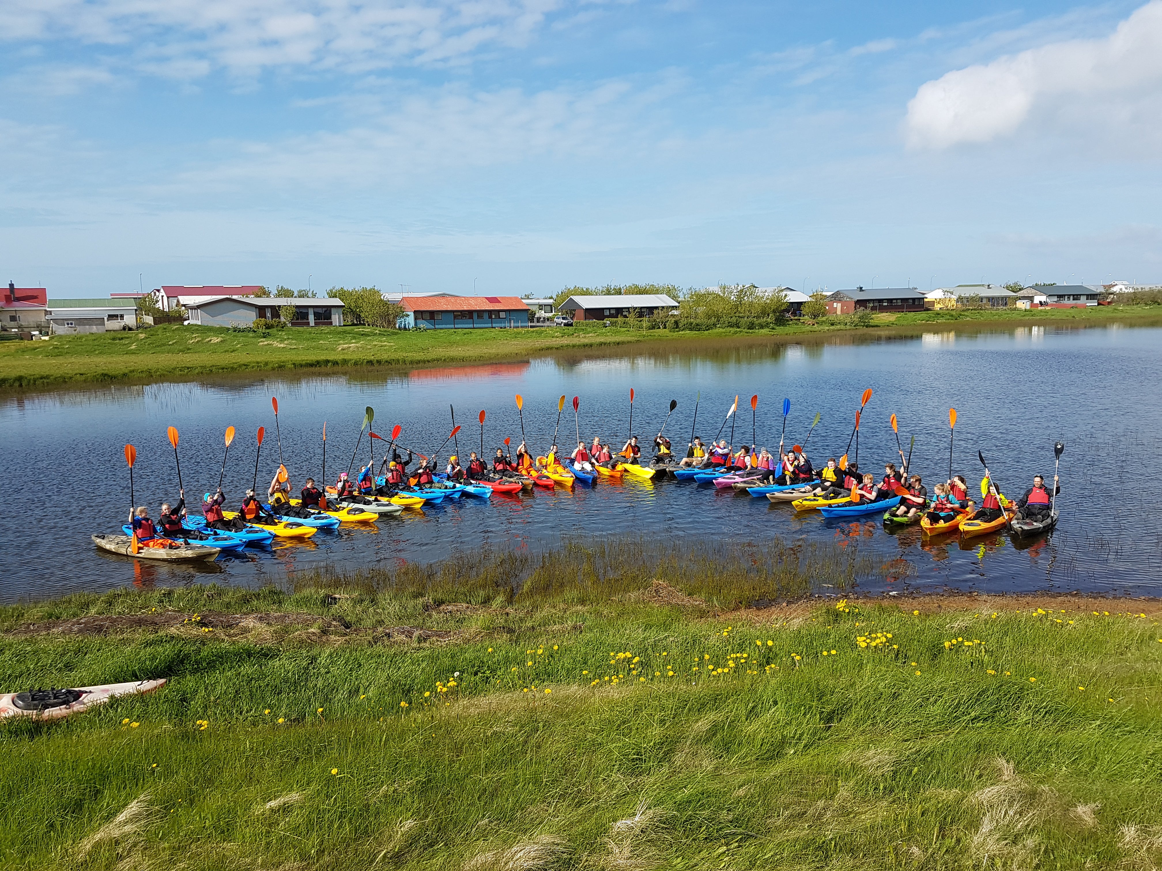 A group of kayakers posing on the water, raising their oars for a photo.