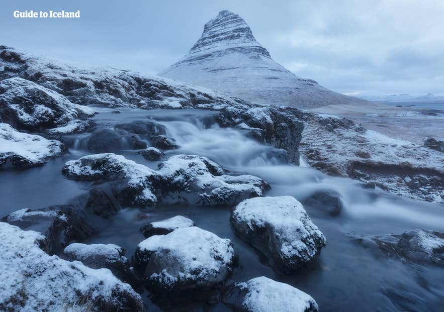 ภูเขาคิร์กจูเฟลล์ (Kirkjufell) และน้ำตกปกคลุมด้วยหิมะในเดือนพฤศจิกายน แสดงอุณหภูมิฤดูหนาวและชั่วโมงกลางวันที่น้อย