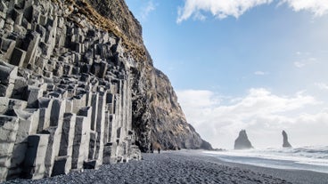 Plaża Reynisfjara z czarnym piaskiem i bazaltowymi kolumnami w słoneczny dzień.