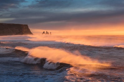 I faraglioni Reynisdrangar in lontananza, mentre le onde si infrangono sulla riva.