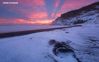 Snö på Reynisfjara svarta sandstrand.