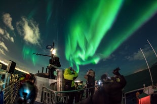 Een groep mensen bewondert en fotografeert het noorderlicht vanaf een boot.