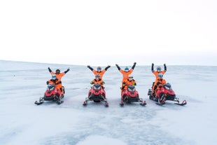 A group of people on snowmobiles on the Langjokull glacier raise their hands above their heads.