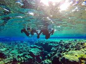 Et par som snorkler, utforsker bunnen av den grunne delen av Silfra-kløften.