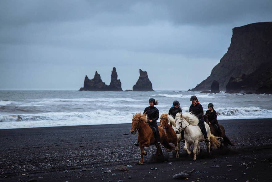 Riders on Reynisfjara black sand beach with the Reynisdrangar sea stacks