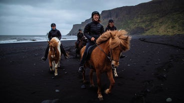 A red horse with a smiling rider moves in a group going at tolt gait over the sands in Vik, South Iceland.
