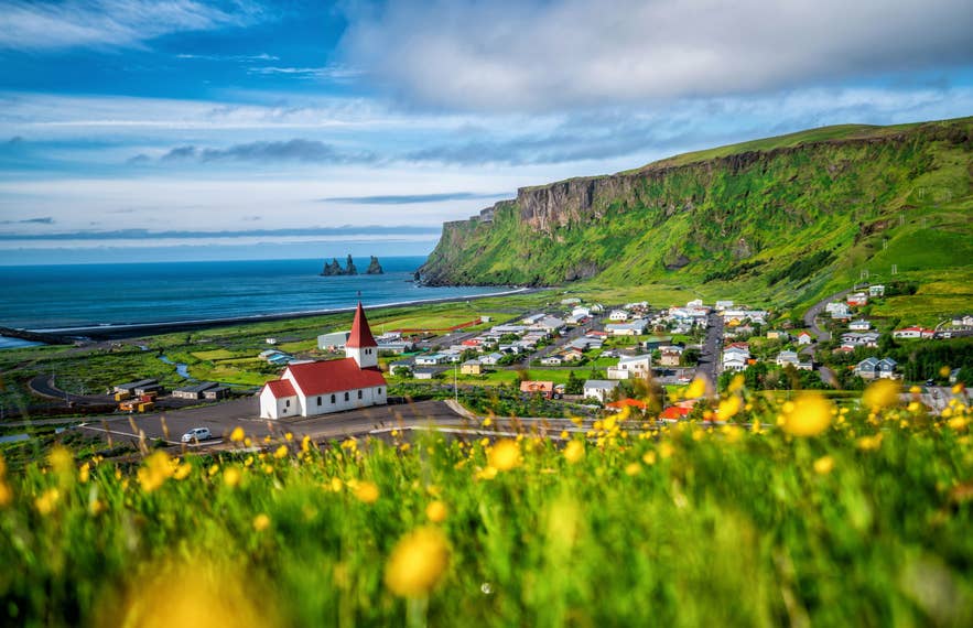 Village of Vik with its white church, green hillsides, and Reynisdrangar sea stacks in May in Iceland.