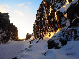 Solen strålar ner på snöiga klippformationer i en ravin i Thingvellir.