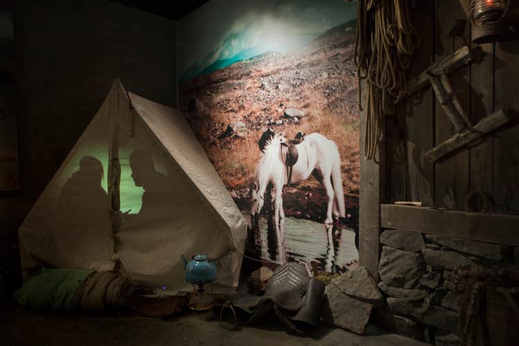 A display of a tent and camping setup in the Wilderness Center exhibition with an image of horse in the background.