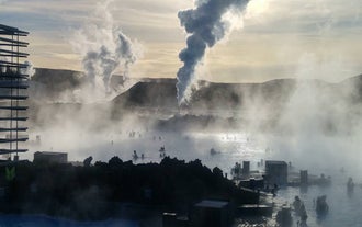 Steam rises into the dusk as travelers bathe in the warm waters of the Blue Lagoon geothermal spa.