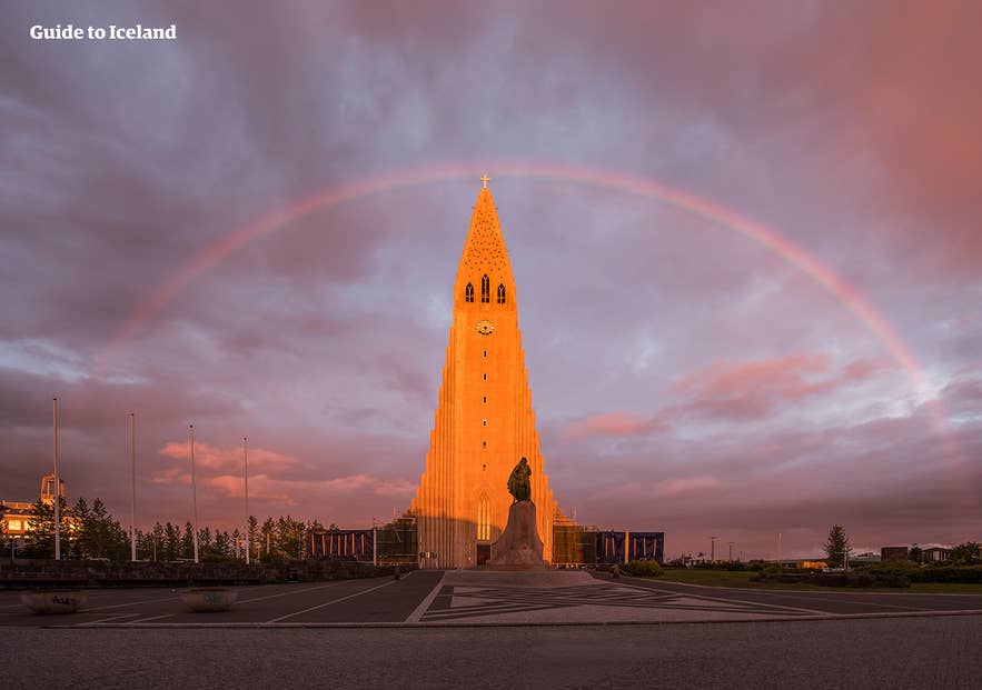 Rainbow arching over Hallgrimskirkja Church in Reykjavik at sunset, with the Leifur Eiriksson statue in front.