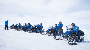 Quatre voyageurs, trois d'entre eux sur des motoneiges, portant des combinaison et casques de sûreté.